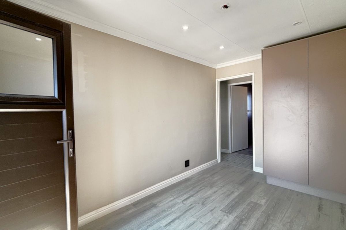 A clean, empty bedroom featuring modern laminate flooring, built-in cupboards, and recessed ceiling lighting, ready for personalization.