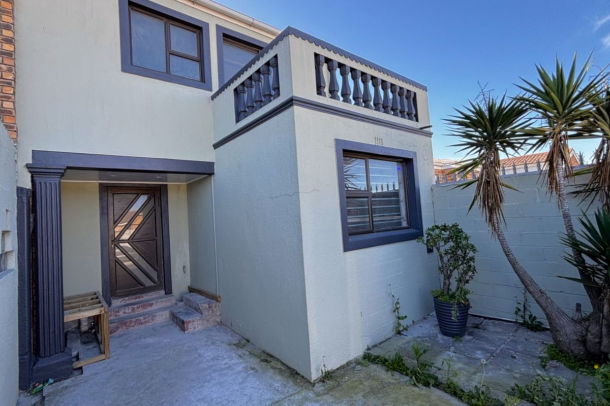 Rear exterior view of the property featuring a small concrete patio, a balcony with a balustrade, and a secure entrance door.