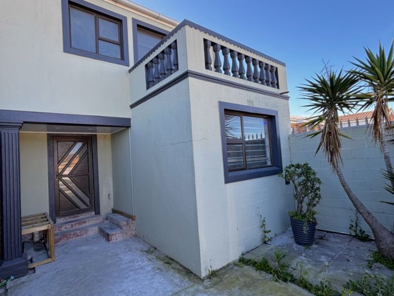 Rear exterior view of the property featuring a small concrete patio, a balcony with a balustrade, and a secure entrance door.