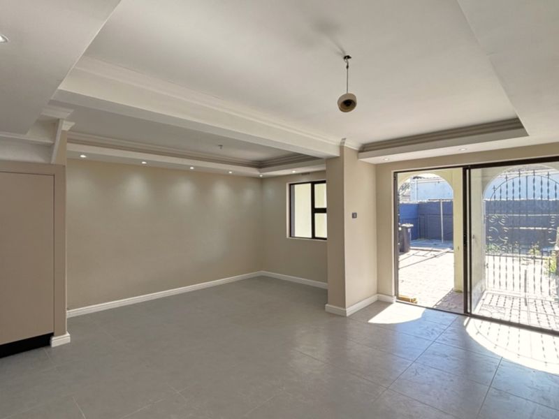 Spacious, empty living area featuring neutral tiled floors, recessed ceiling lighting, and a sliding glass door providing access to the rear patio.