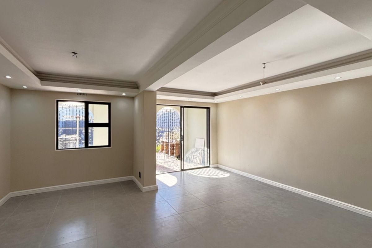 A bright, spacious, and empty living area featuring neutral tiled flooring, a modern tray ceiling with recessed lighting, and access to an outdoor patio.