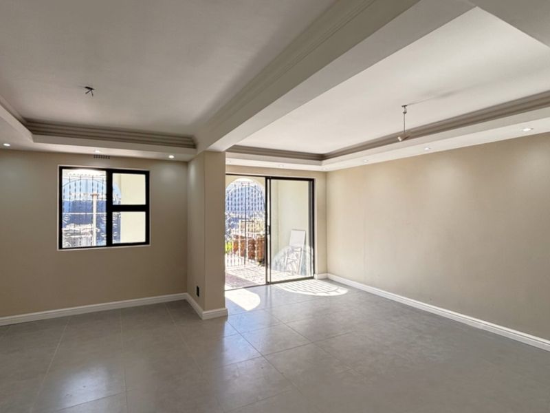 A bright, spacious, and empty living area featuring neutral tiled flooring, a modern tray ceiling with recessed lighting, and access to an outdoor patio.