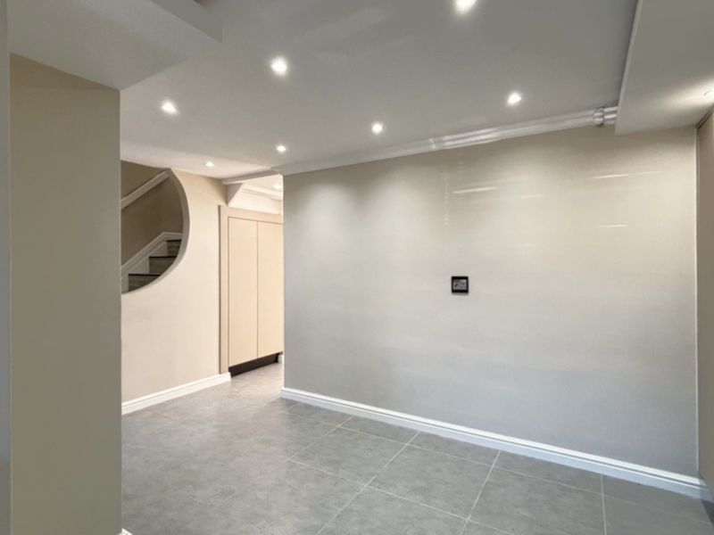 A modern, well-lit hallway featuring neutral tones, tiled flooring, recessed lighting, and a distinctive curved architectural opening leading to the staircase.