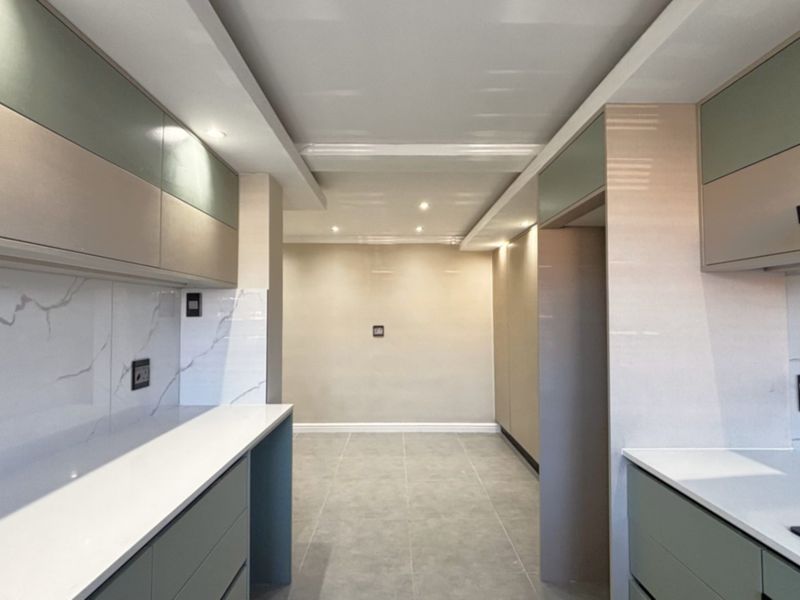 A modern, empty kitchen featuring sleek two-tone cabinetry, stone countertops, marble-look splashbacks, and integrated extractor fan with recessed ceiling lighting.
