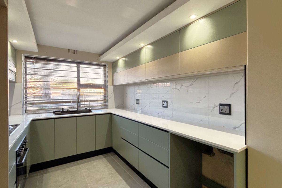 Modern, renovated kitchen featuring sleek sage green cabinetry, white quartz countertops, marble-look tile backsplash, and integrated built-in appliances.