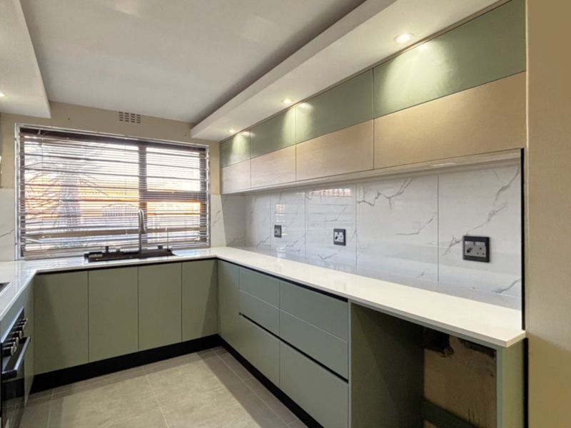 Modern, renovated kitchen featuring sleek sage green cabinetry, white quartz countertops, marble-look tile backsplash, and integrated built-in appliances.