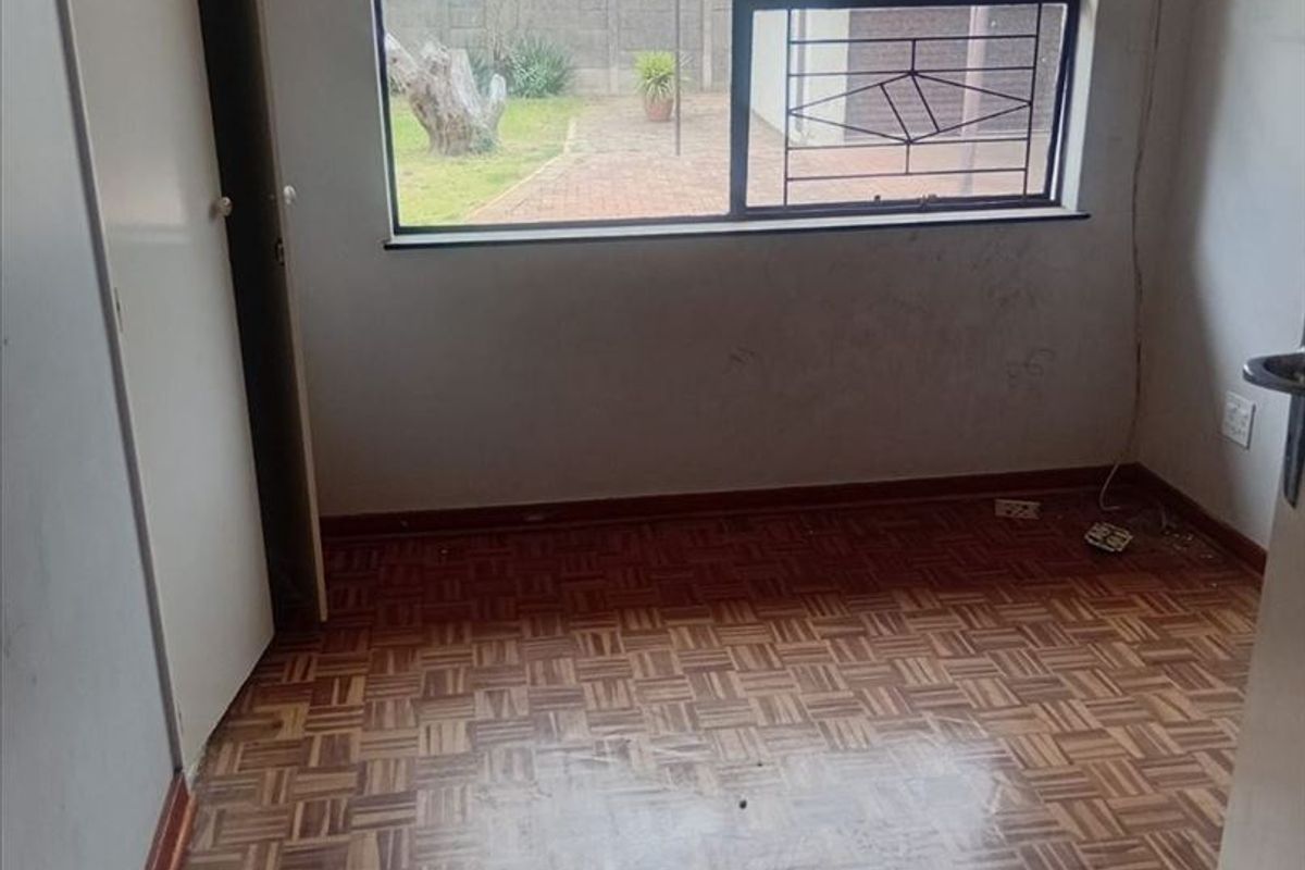 An empty bedroom featuring original parquet flooring, a built-in cupboard, and a window with security bars overlooking the rear garden area.