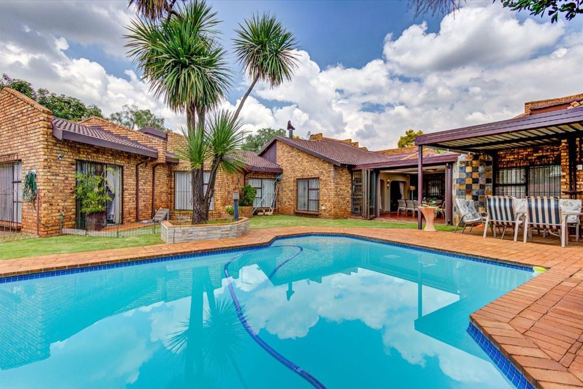 A well-maintained outdoor entertainment area featuring a swimming pool, brick paving, and a covered patio attached to a face brick house.