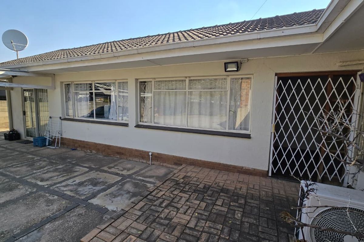 Rear exterior view of the property featuring a paved patio area, security gate, and tiled roof.