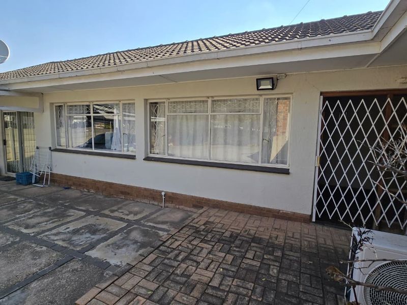 Rear exterior view of the property featuring a paved patio area, security gate, and tiled roof.