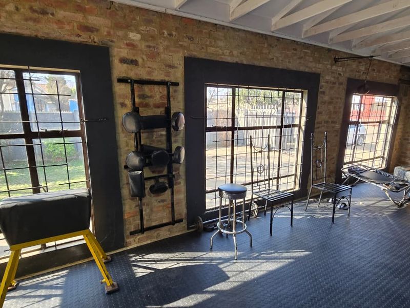 A dedicated home gym space featuring exposed brick walls, industrial-style steel-framed windows with security bars, and durable rubber flooring under exposed timber ceiling beams.