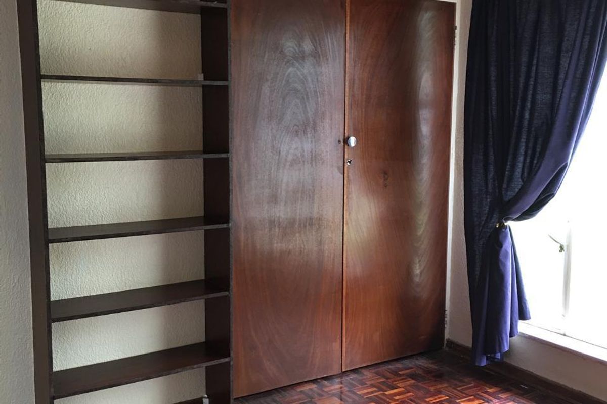 Bedroom featuring original parquet flooring, built-in wooden cupboards, and an integrated shelving unit, offering a classic foundation for renovation.