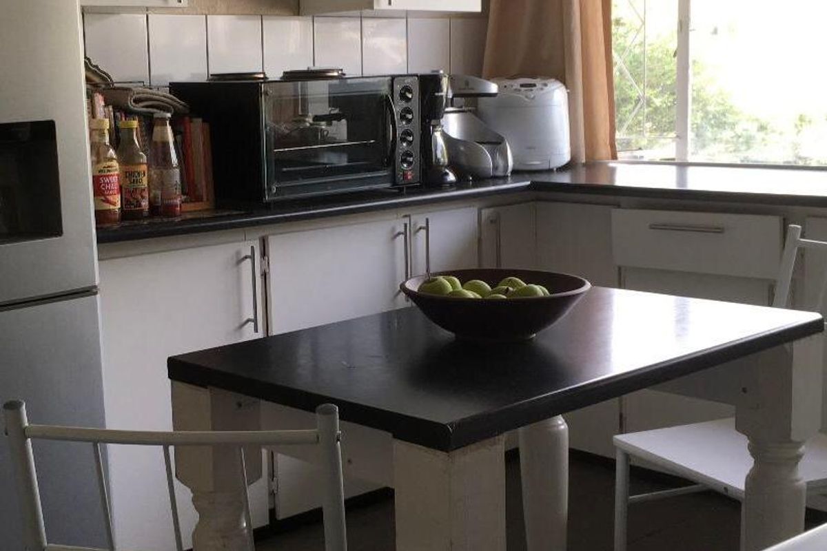 A functional kitchen featuring white cabinetry, dark countertops, tiled backsplash, and tiled flooring, with natural light provided by a window with security bars.