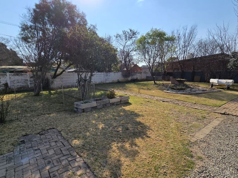 Spacious rear garden featuring brick pathways, a gravel area, and a perimeter wall, offering potential for landscaping and outdoor improvement.