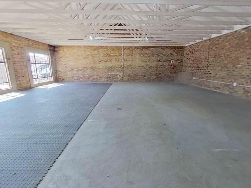 A spacious, empty garage or utility space featuring exposed brick walls, industrial-style windows, and exposed timber roof trusses.