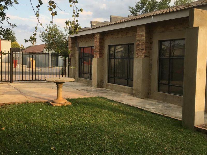 Rear exterior view of the property featuring a concrete patio, lawn area, and secure metal fencing with exposed brick and concrete architectural details.