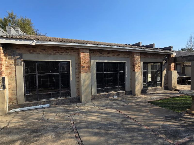 Rear view of the property featuring an exposed brick facade, steel-framed windows, and a paved patio area.