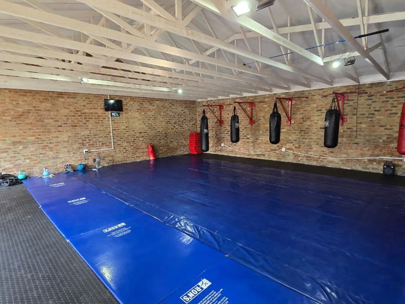 A dedicated home gym space featuring exposed brick walls, high timber truss ceilings, and durable rubber flooring with wall-mounted training equipment.