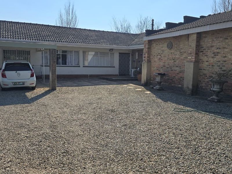 Front exterior view of the house featuring a gravel driveway, a covered carport, and a traditional brick facade with a tiled roof.