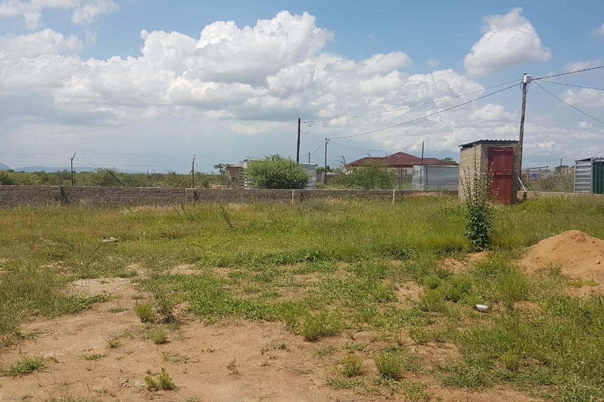 A large, undeveloped plot of land featuring a perimeter wall, a small brick outbuilding, and overhead power lines.