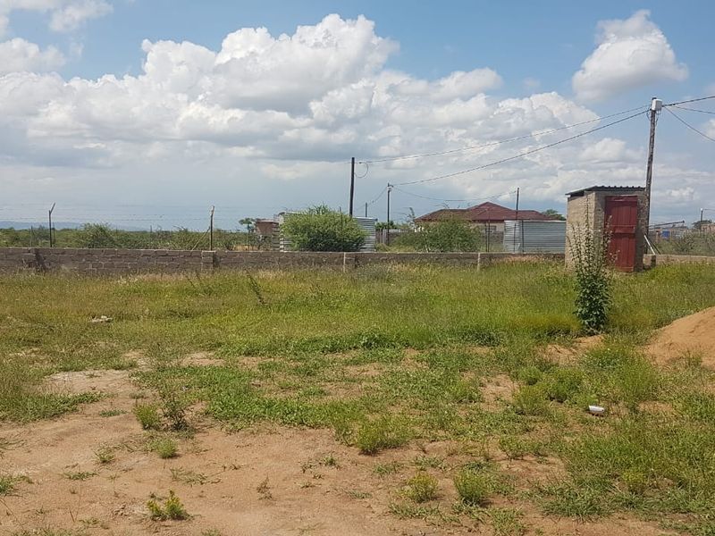 A large, undeveloped plot of land featuring a perimeter wall, a small brick outbuilding, and overhead power lines.