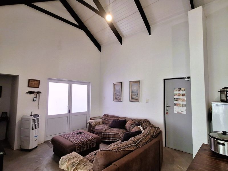 Open plan living area featuring a high vaulted ceiling with exposed timber beams, concrete flooring, and double glass doors leading to the exterior.