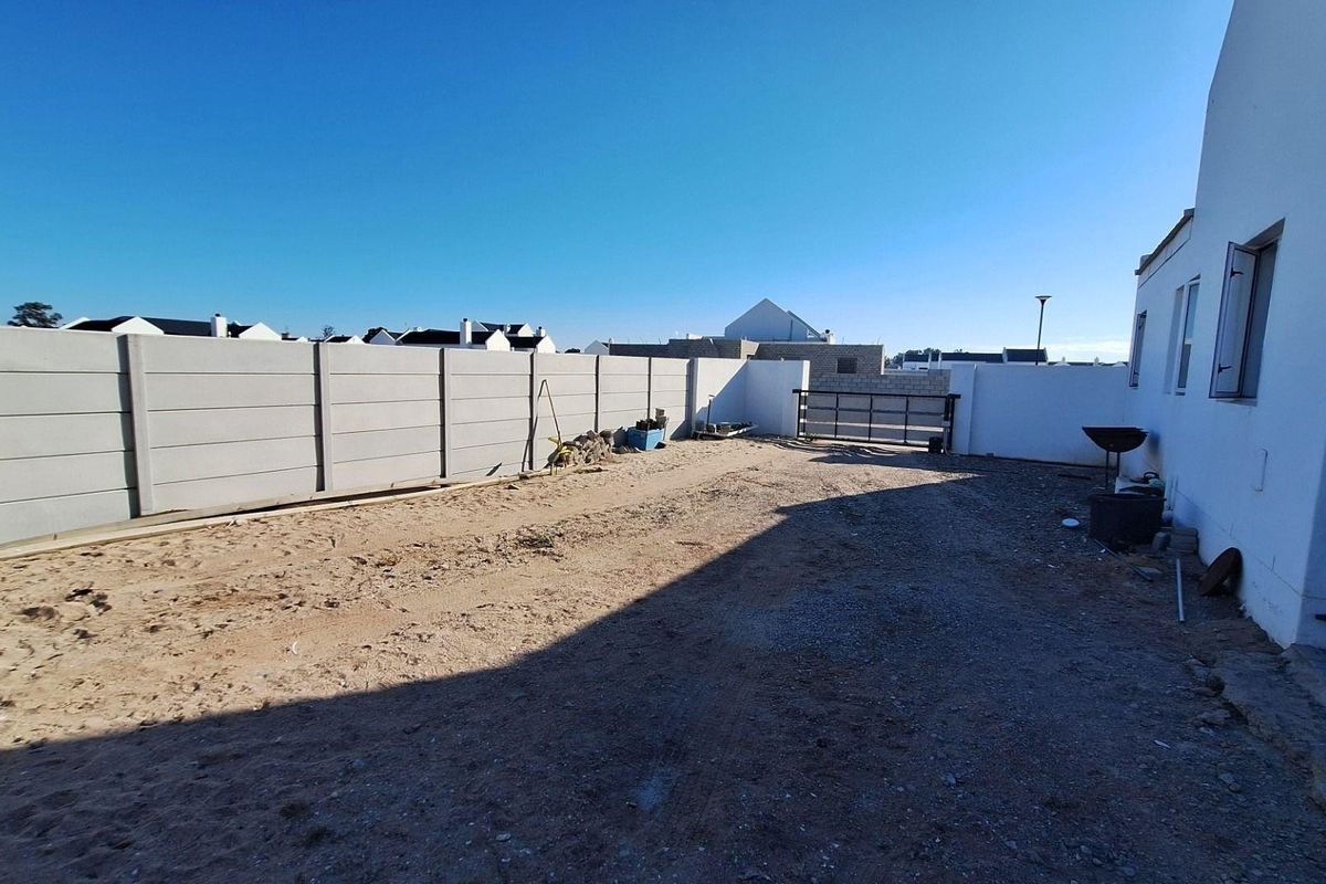 A spacious, unlandscaped rear yard featuring a precast concrete boundary wall and gated access, offering significant potential for garden development.
