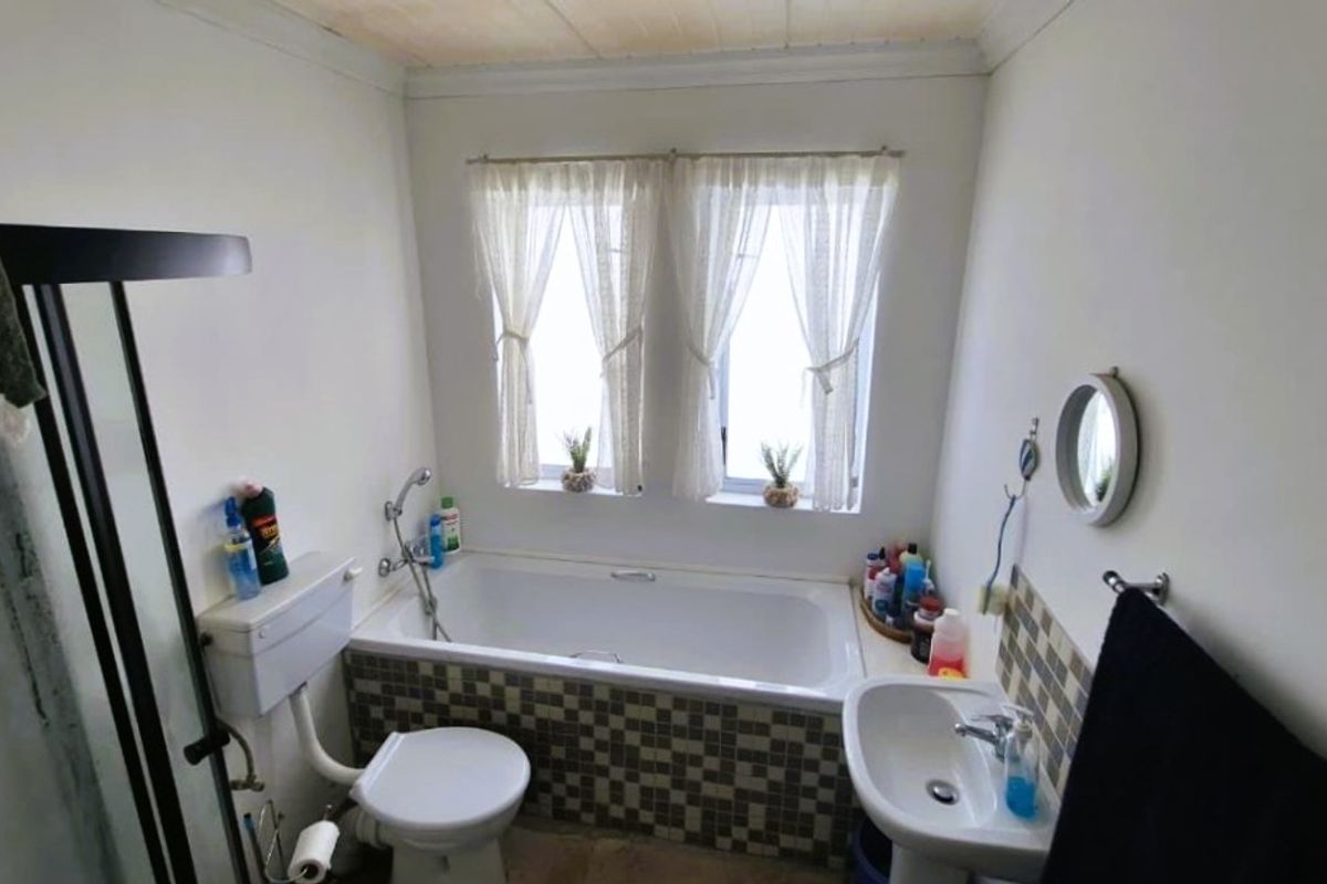 A functional bathroom featuring a bathtub with mosaic tile surround, a pedestal sink, a toilet, and a separate shower enclosure.
