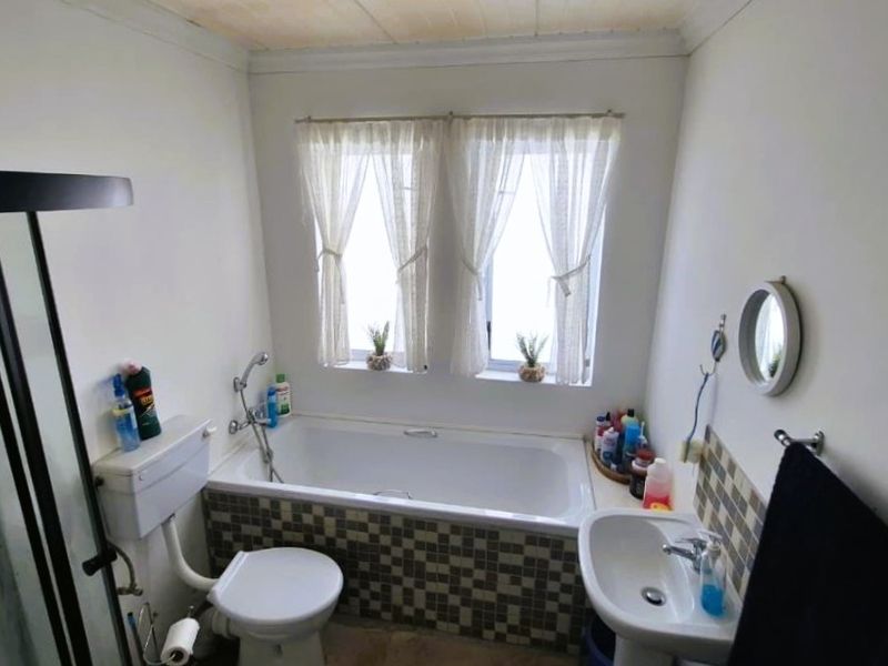 A functional bathroom featuring a bathtub with mosaic tile surround, a pedestal sink, a toilet, and a separate shower enclosure.