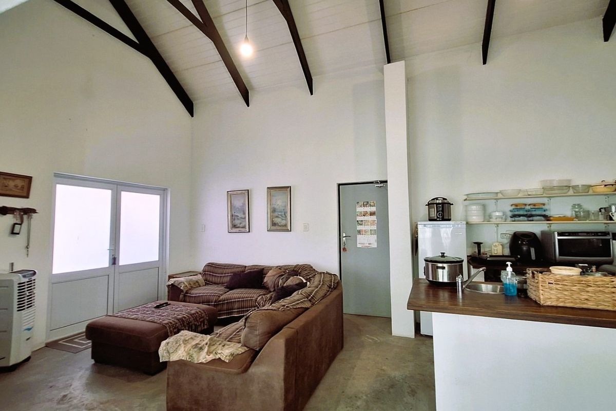 Open-plan living area featuring a high vaulted ceiling with exposed timber beams, integrated kitchen space with open shelving, and direct access to the outdoors.