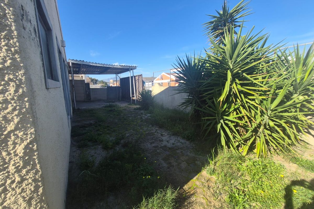 Rear exterior area featuring a carport, boundary wall, and paved space with significant potential for landscaping and outdoor improvement.