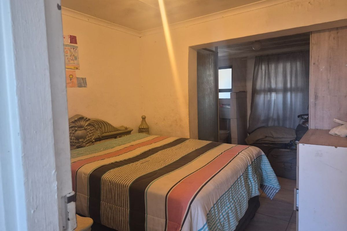 A bedroom featuring tiled flooring and an adjoining en-suite bathroom, requiring cosmetic updates to wall and ceiling finishes.