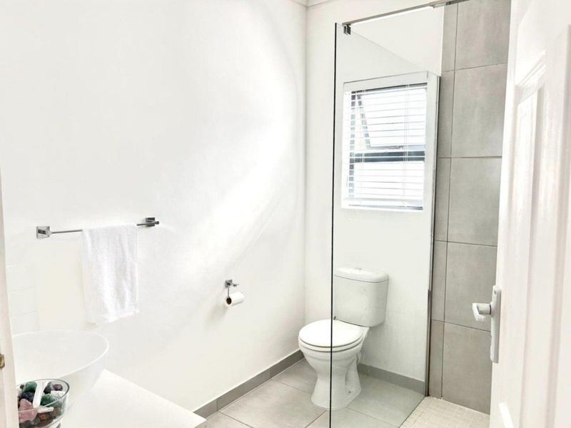 A modern bathroom featuring a glass-enclosed shower, neutral grey floor tiles, and a contemporary vessel sink setup.