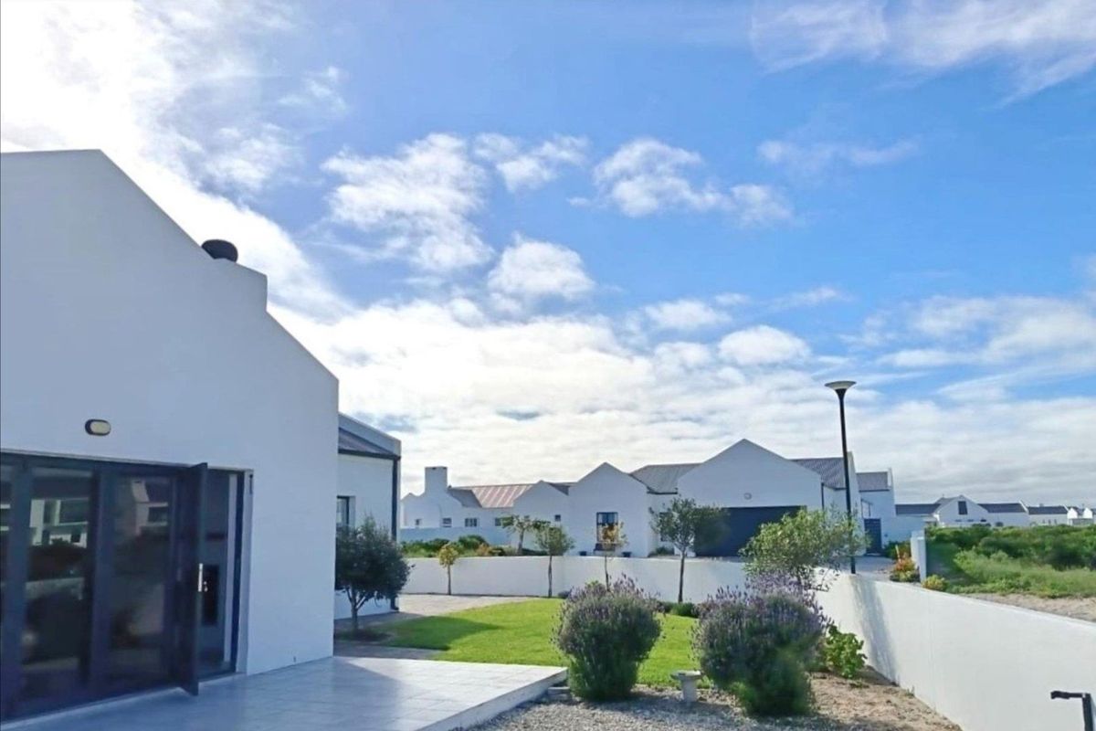 A well-maintained rear exterior view featuring a tiled patio, landscaped garden, and white boundary walls in a modern residential estate setting.