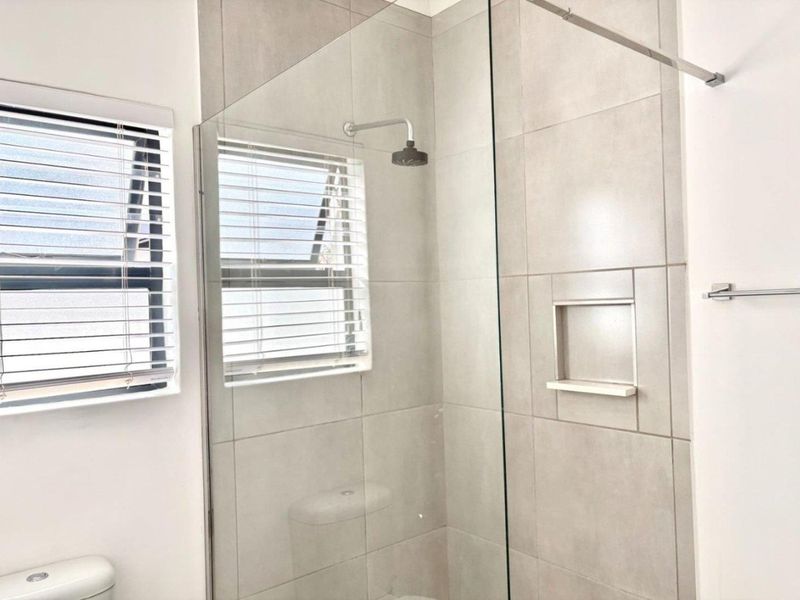A modern bathroom featuring a glass-enclosed shower with a built-in niche, neutral wall tiles, and a clean, functional layout.