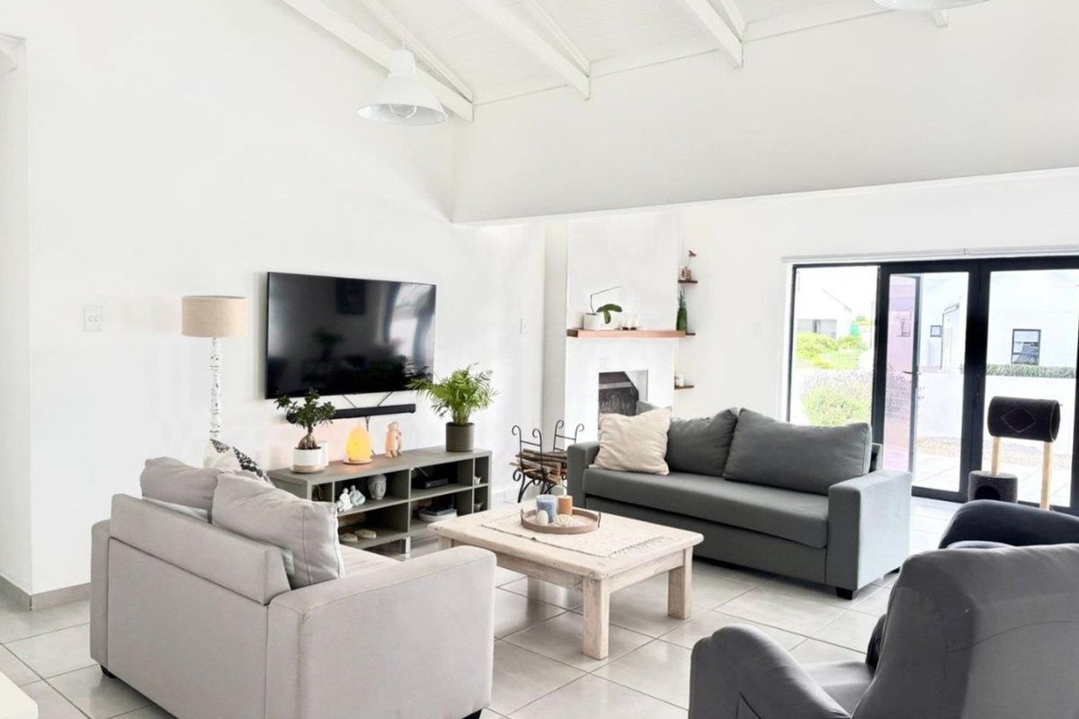 Bright and airy living room featuring a vaulted ceiling with exposed beams, tiled flooring, a fireplace, and large sliding glass doors leading outdoors.