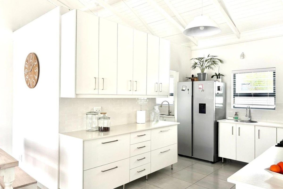 Modern kitchen featuring white cabinetry, stone countertops, subway tile backsplash, and an exposed beam ceiling, creating a bright and functional culinary space.