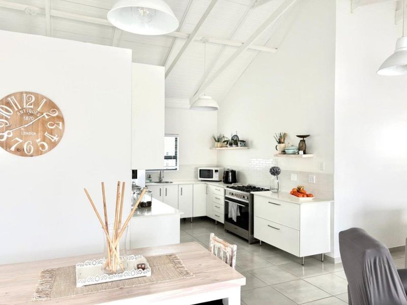 Bright open-plan kitchen featuring white cabinetry, stone countertops, subway tile backsplash, and high vaulted ceilings with exposed beams.