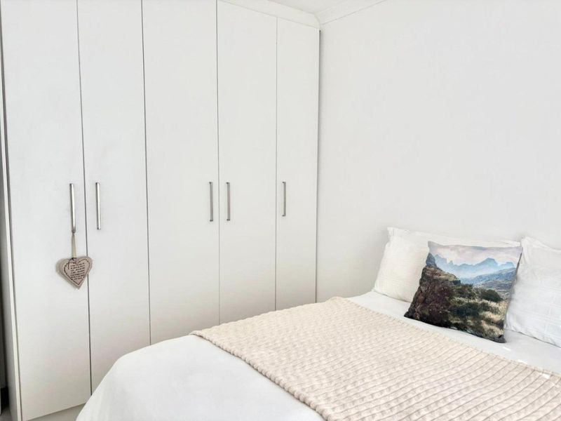 A clean and bright bedroom featuring floor-to-ceiling built-in cupboards with modern handles.