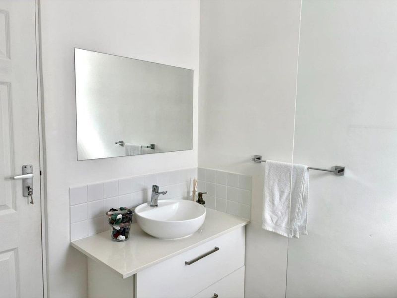 A clean and modern bathroom vanity area featuring a white vessel sink, stone-look countertop, wall-mounted mirror, and minimalist chrome fixtures.