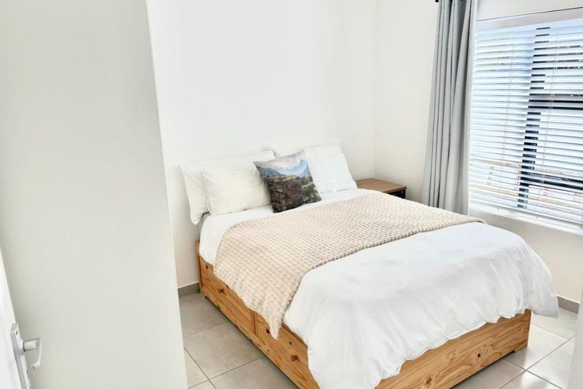 A bright and neutral bedroom featuring tiled flooring and window blinds, offering a clean and simple living space.
