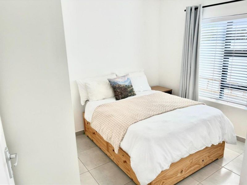 A bright and neutral bedroom featuring tiled flooring and window blinds, offering a clean and simple living space.