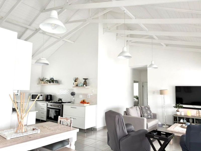 Bright open-plan living and kitchen area featuring high vaulted ceilings with exposed trusses, modern cabinetry, and tiled flooring throughout.
