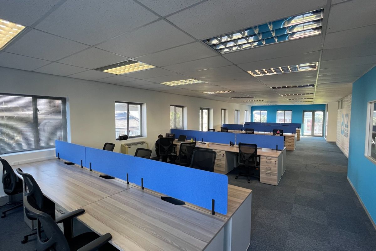 Spacious open-plan commercial office area featuring modular desk configurations, suspended ceilings with recessed lighting, and carpeted flooring throughout.