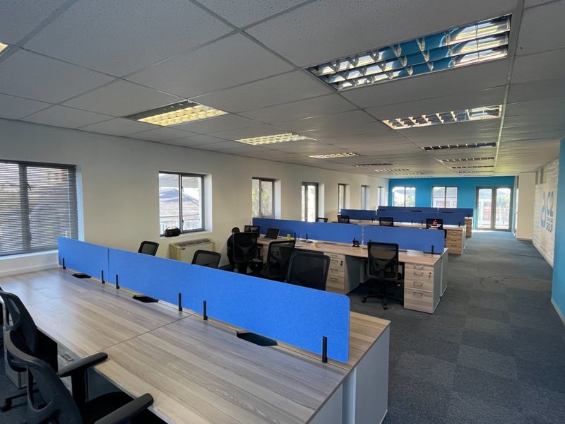 Spacious open-plan commercial office area featuring modular desk configurations, suspended ceilings with recessed lighting, and carpeted flooring throughout.