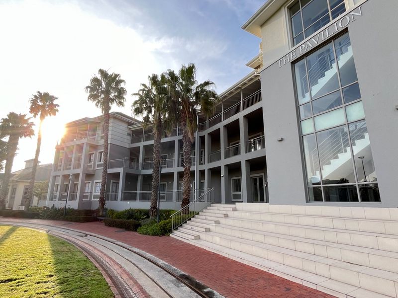 Exterior view of The Pavilion commercial building featuring a modern multi-story facade with glass windows, metal railings, and stone entrance steps.