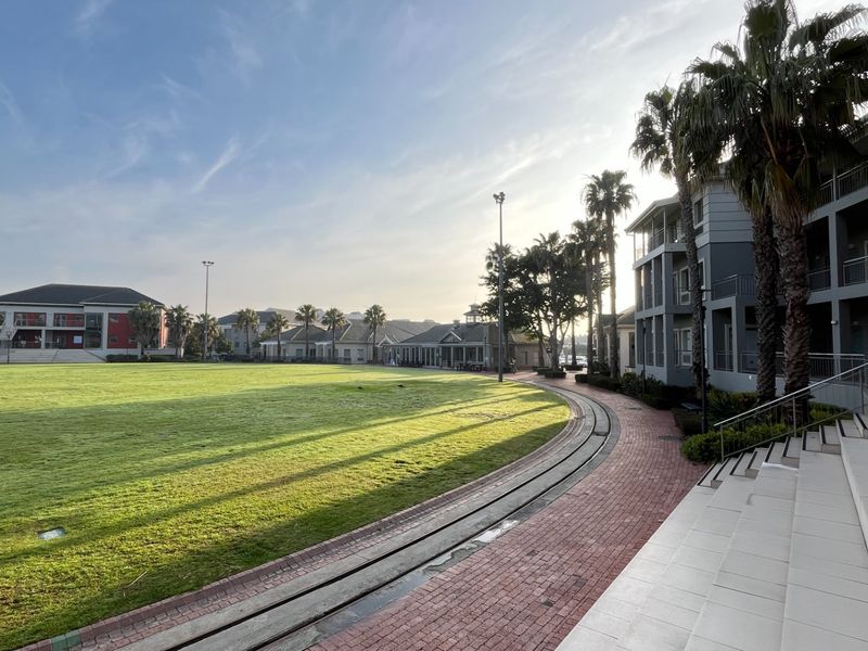 A wide-angle view of a commercial property complex featuring a large central lawn, paved walkways, and multi-story building facades with external staircases.