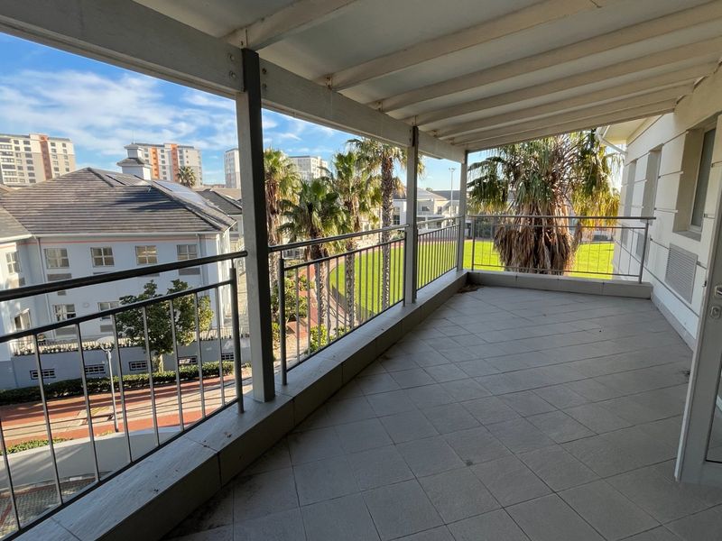 A spacious covered balcony featuring tiled flooring, a metal safety balustrade, and views over the surrounding commercial estate.