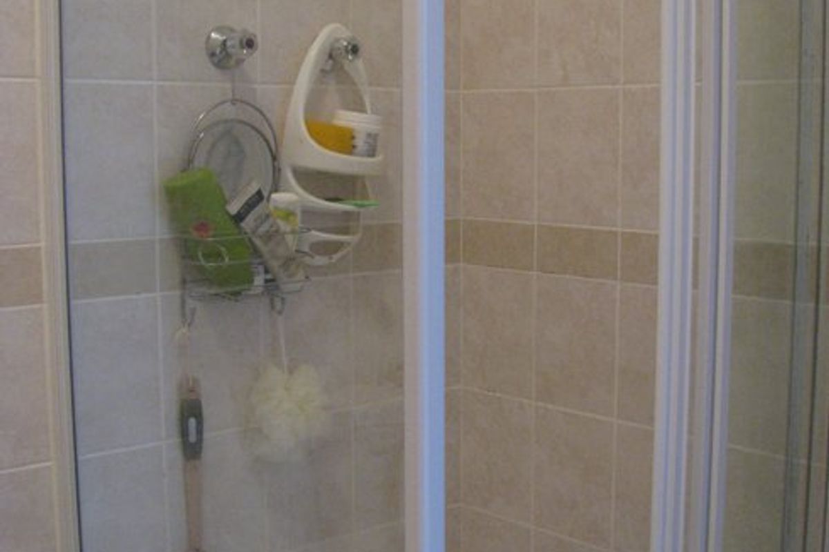 A functional shower enclosure featuring tiled walls and a standard shower tray, showing signs of wear consistent with age.