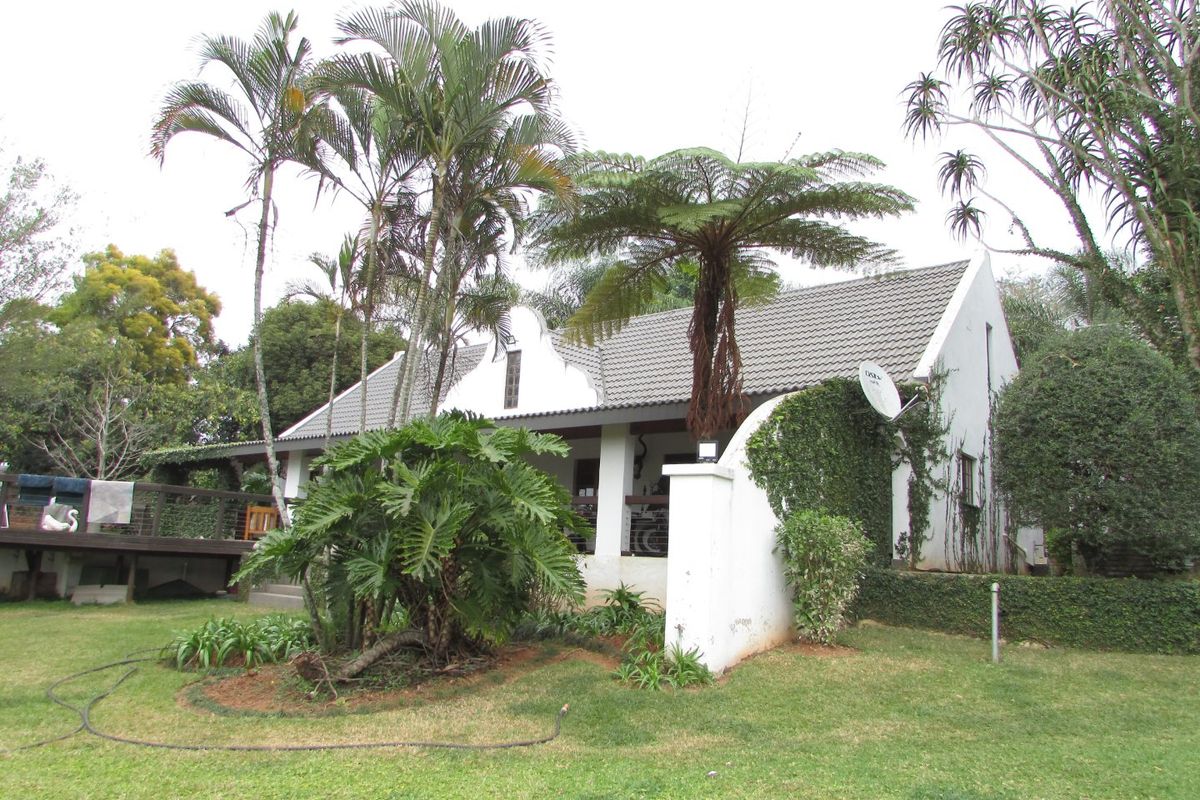 Rear view of a house featuring a tiled roof, a covered patio, and a raised timber deck set within a mature landscaped garden.